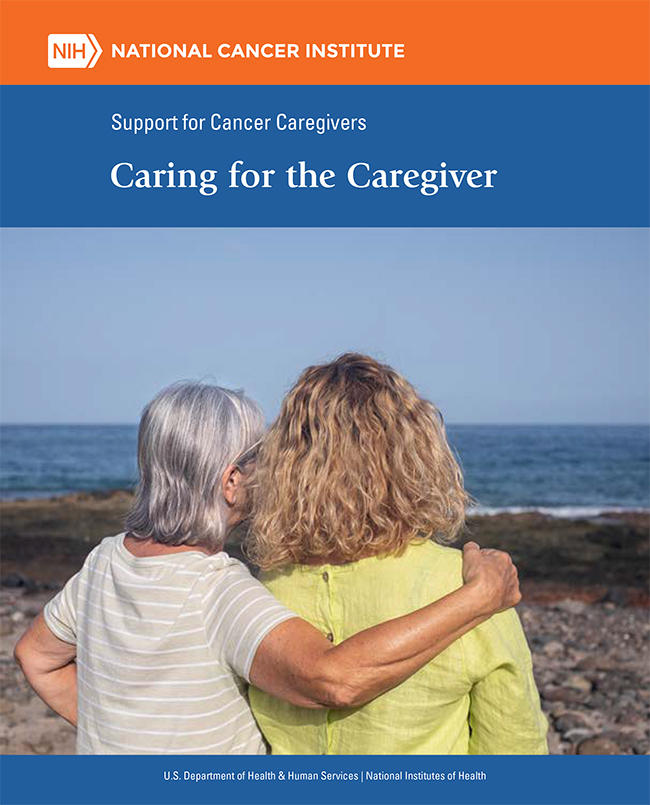 Older woman with her arm around younger woman with their backs to the camera looking at the ocean.
