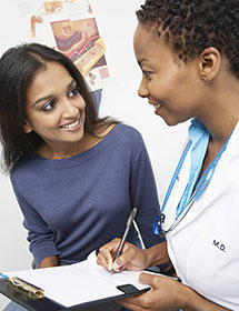 Doctor and patient having a consultation, with the doctor taking notes while engaging in conversation with the patient in a clinical setting.