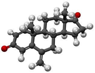 3D molecular model of exemestane showing its chemical structure with black carbon atoms, white hydrogen atoms, and red oxygen atoms arranged in the characteristic steroid-like ring structure of this cancer therapy drug.