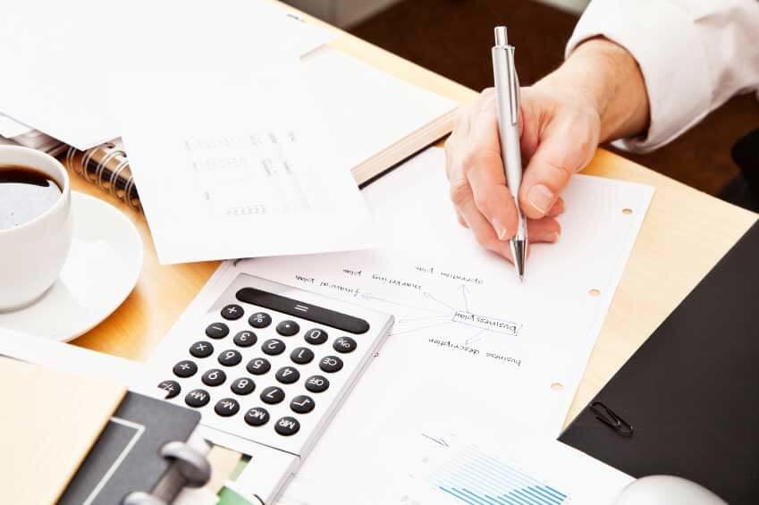 Person brainstorming on paper with a calculator and coffee on the desk