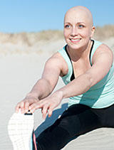 Woman who has undergone chemo and is bald in athletic wear sitting outdoors against a bright blue sky background