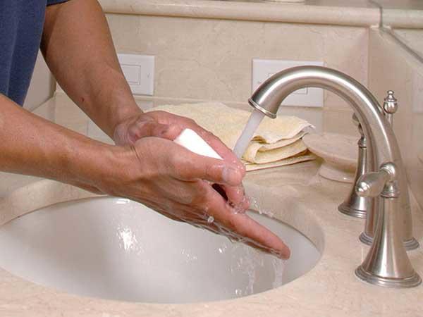 Person washing hands with soap and running water at a sink.
