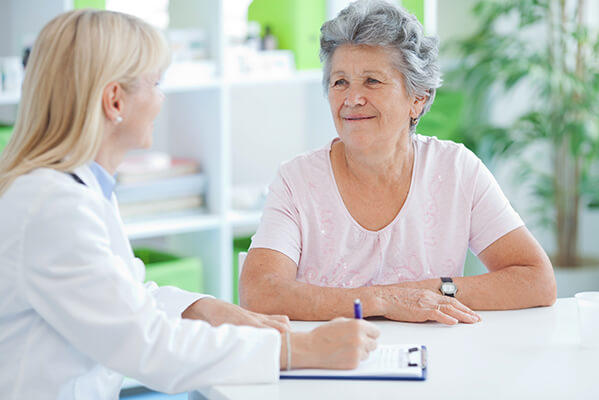 Medical professional writing notes and talking to a patient.