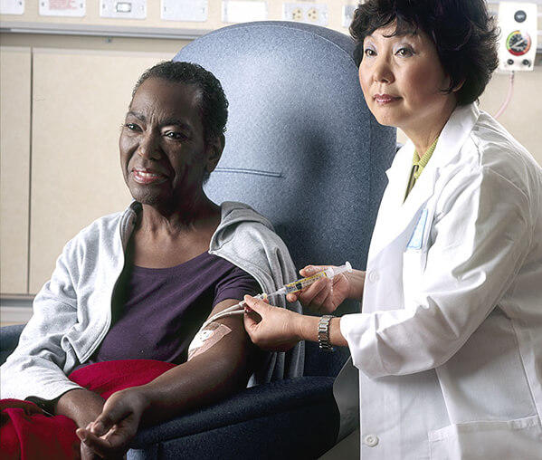 Seated female patient receives chemotherapy infusion from female nurse.