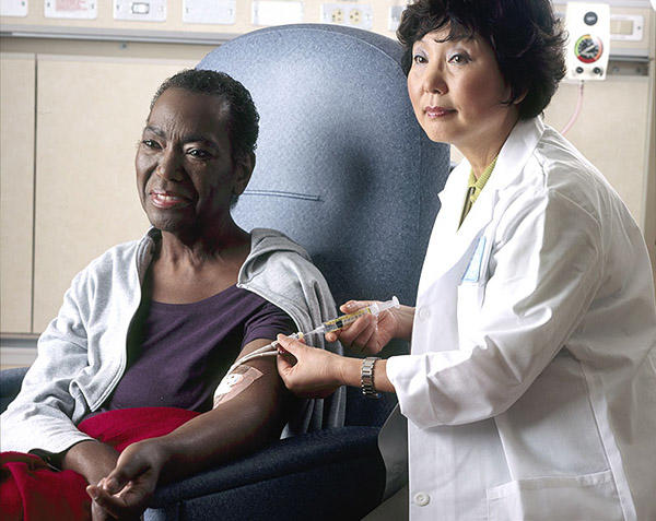 Seated female patient receives chemotherapy infusion from female nurse.
