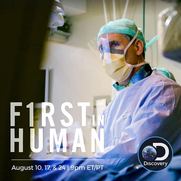 A doctor in an operating room wears a plastic face shield, a mask, scrubs and a green cap. He looks off into the distance. In the bottom left corner, text reads “F1RST in HUMAN” with the dates and times of August 10, 17 & 24, 9pm ET/PT. The Discovery Channel logo is on the bottom right corner.