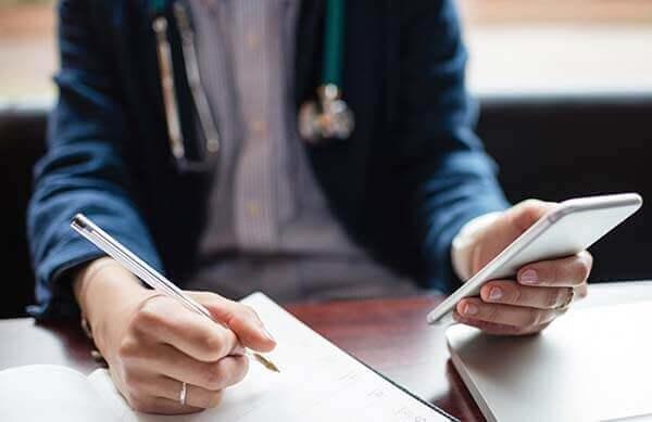 A medical professional writing and using a mobile phone.