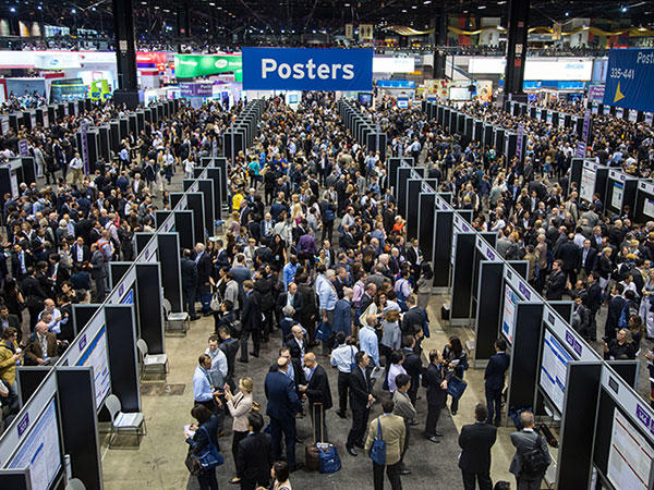 A birds-eye view of a large crowd at a conference. There are four rows with posters on them spanning with width of the hall. Above the crowd and the posters is a blue sign with the word “Posters”. There are hundreds of people in the crowd.