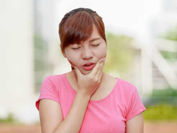 Woman in a pink shirt touching her jaw area with a pained expression