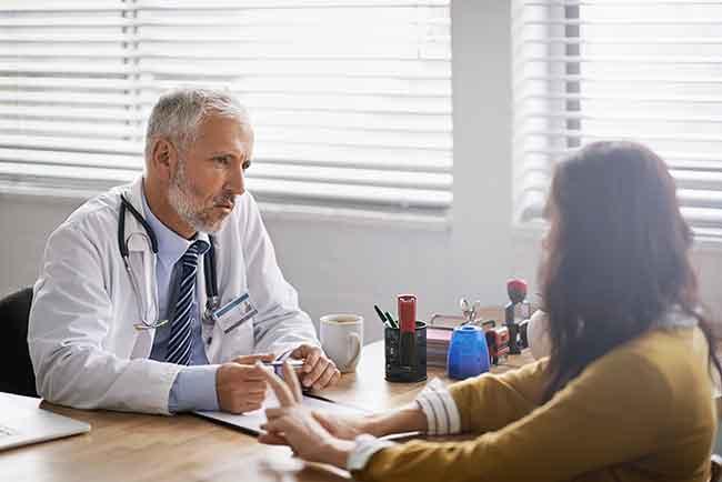 Seated male doctor conversing with seated female patient