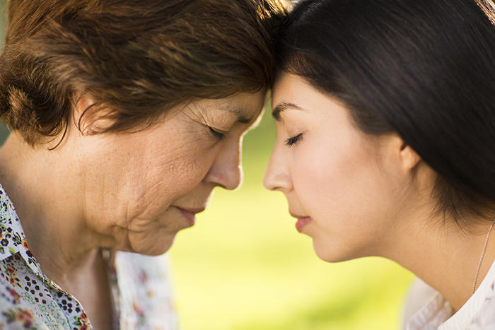 Mother and daughter together with heads bowed, foreheads touching