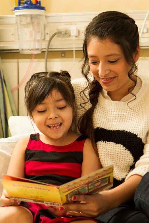 Two sisters sitting side by side reading in a hospital bed