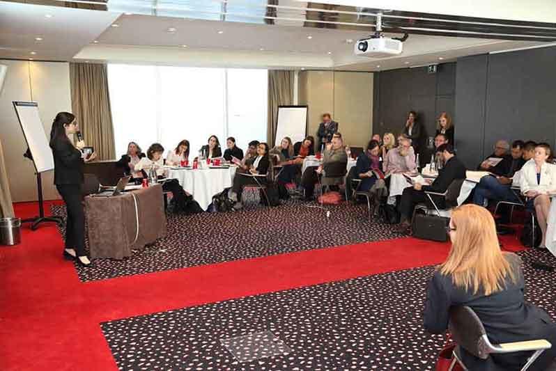 A group of people sitting at tables in a conference room watching a presenter.