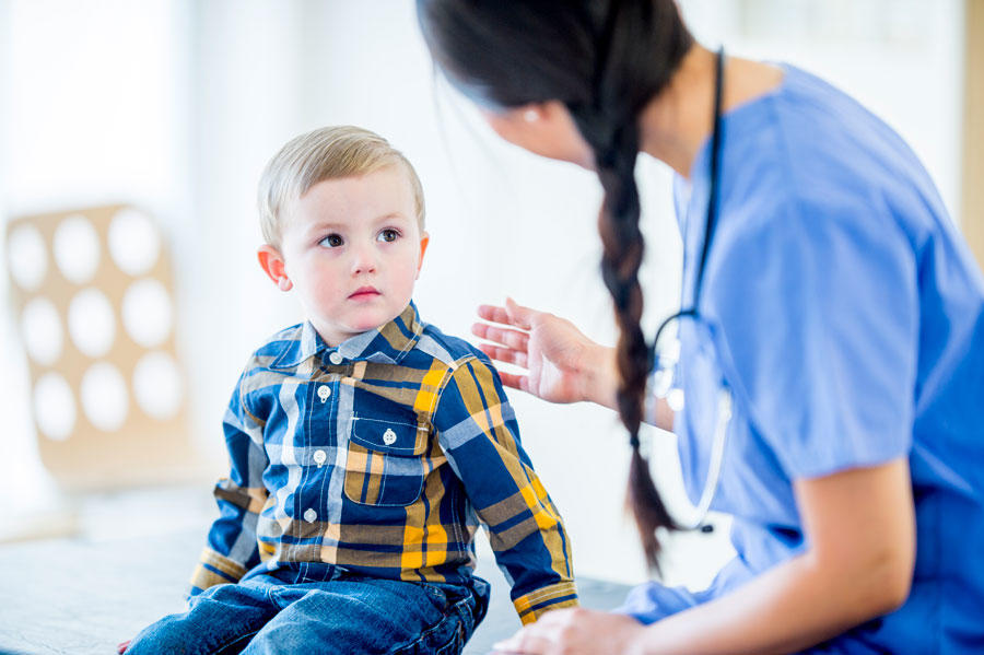 Female health care provider talks to young boy seated next to her.
