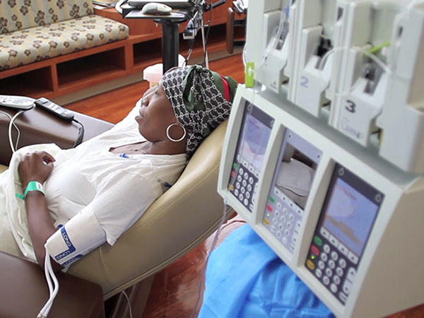 Woman wearing headscarf and reclining in chair receives cancer treatment at medical facility.