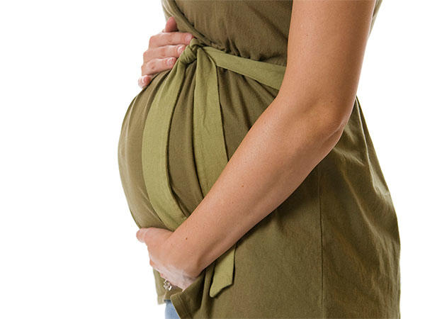 A close-up of a woman’s arms holding her pregnant stomach. She is wearing a dark olive-colored dress.