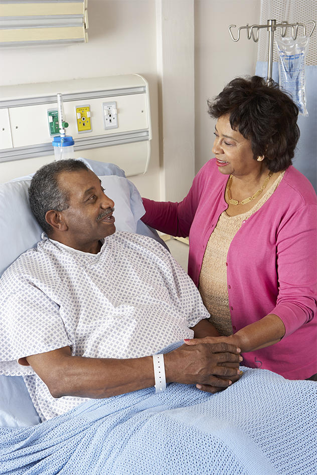Woman visits male patient who is sitting up in a hospital bed.