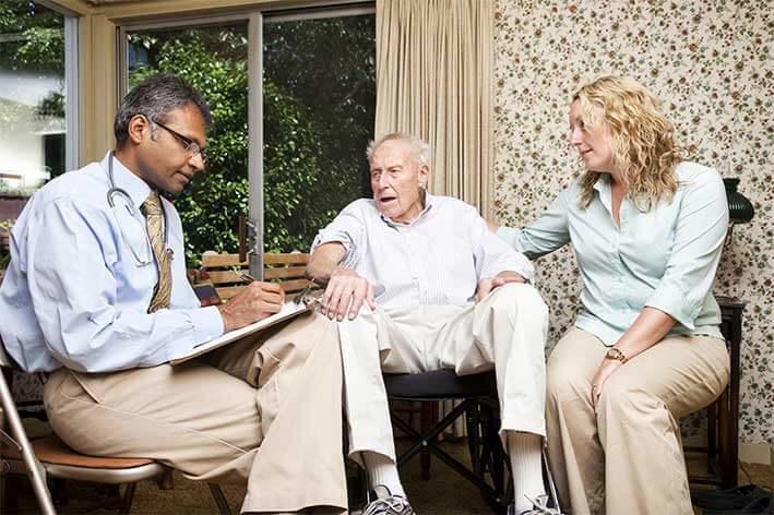 Male health care provider meets with senior male patient and a female caregiver at home.