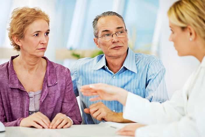 Man and woman seated together listen intently as female doctor speaks to them.
