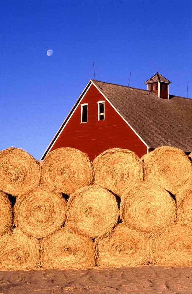 Roof of a red farmhouse with hay bales in the foreground.