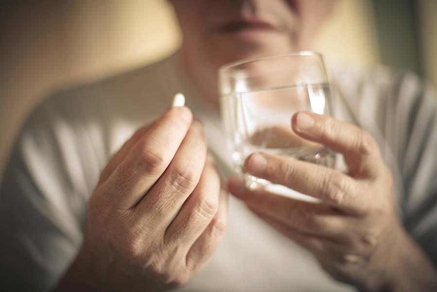 A person with oral medication in one hand and a glass of water in the other hand.