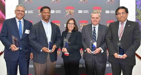 Five CURE scholars standing together, each holding an award for lifetime achievement.