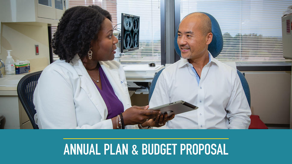 A doctor speaks to a patient in her office. The doctor is a Black woman with shoulder length hair, a white coat, a purple blouse, and jewelry. She is holding a tablet. The patient is a bald Asian man wearing a white button up shirt. Both are sitting and wear happy expressions. In the background, a scan can be seen on the computer screen, along with windows and cabinets. Text at the bottom reads “Annual Plan & Budget Proposal”.