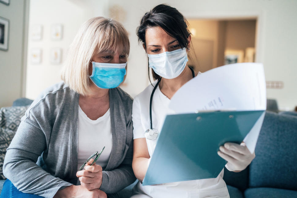A nurse wearing a face mask talking with an older female patient wearing a face mask.