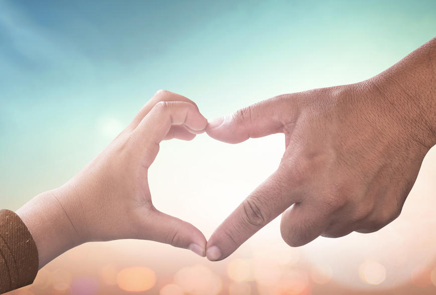 Close-up of child and adult hands joining fingertips to form heart shape