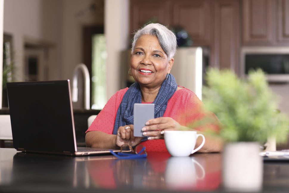 Woman sitting in front of a laptop and holding a smart phone.