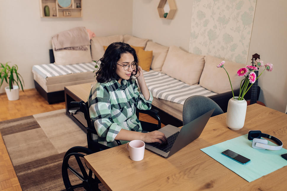 Young woman in a wheelchair talking on phone from her home office