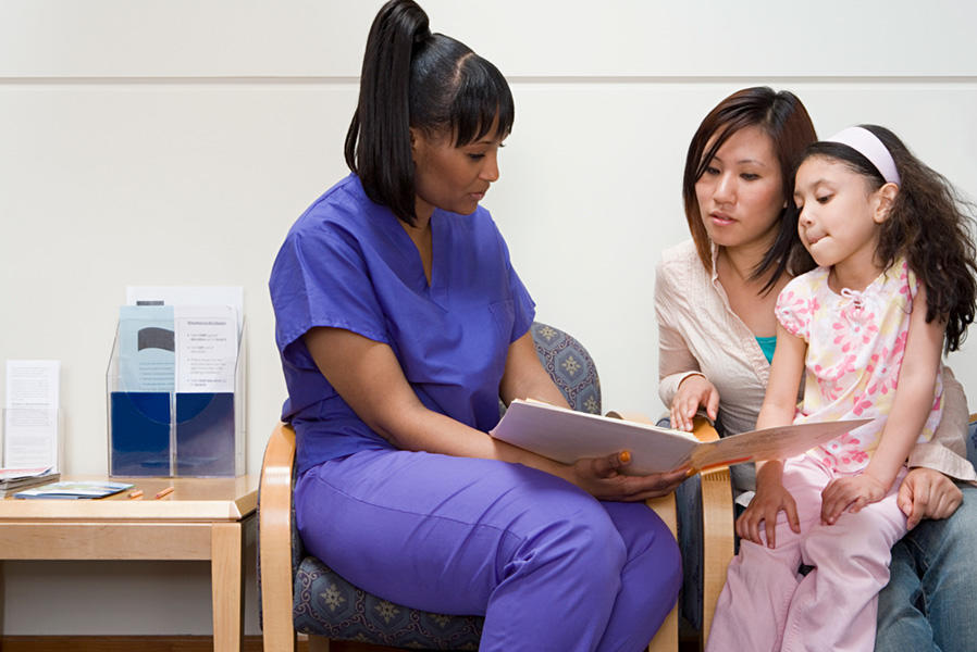 Black nurse reads book to daughter sitting on a mother’s lap