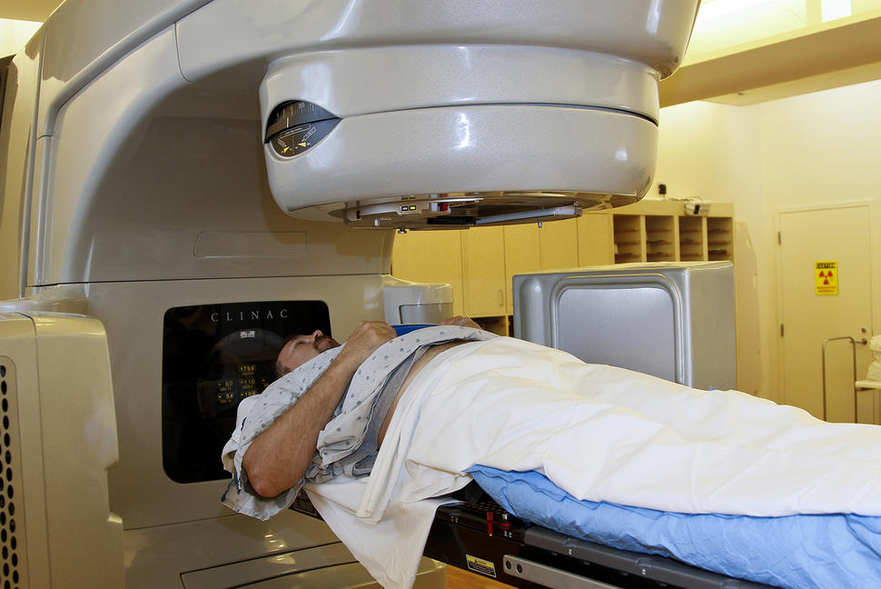 A patient model is positioned on a linear accelerator (LINAC) table to undergo radiation therapy for prostate cancer. The blue vacuum mold helps hold his body steady during treatment.