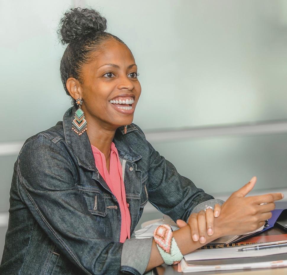 Dr. Lauren E. McCullough, shown sitting, rests her arms on a small stack of books and papers while speaking happily.