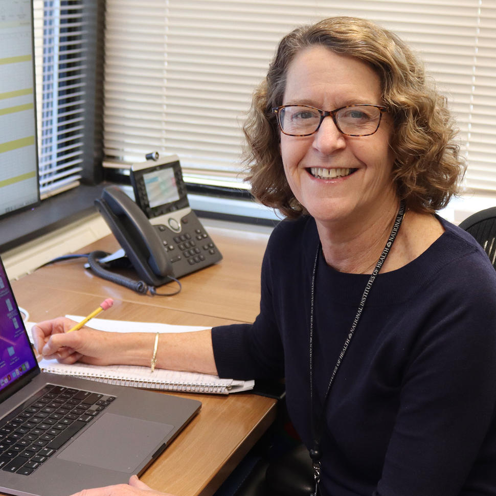 Pamela Wolters sits at a desk with her laptop open and a pencil in her hand.