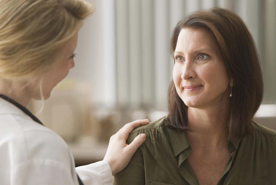 A doctor with her hand on a smiling patient's shoulder while talking to her.