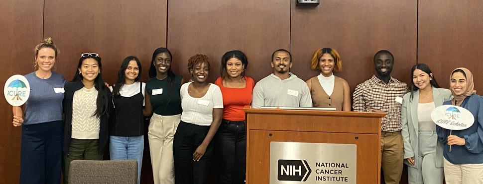 New iCURE scholars gather around the podium at the 2023 iCURE NCI Shady Grove Campus Orientation.