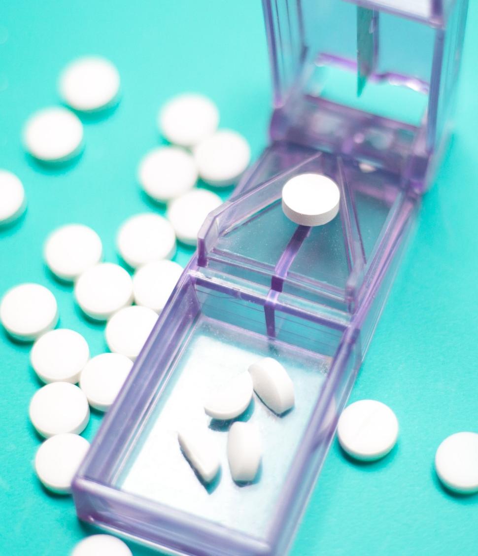 An image of white pills in a gray, plastic pill cutter