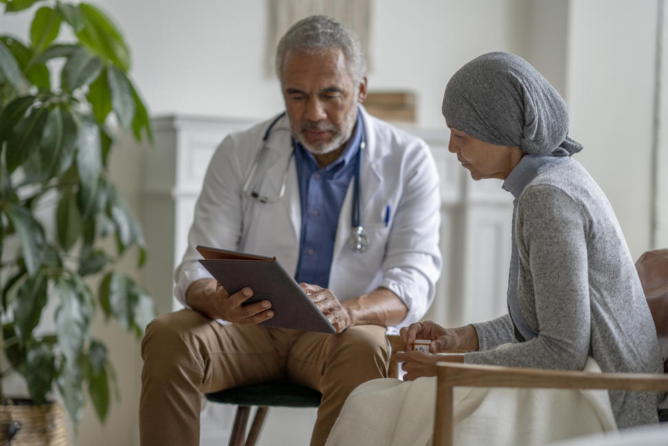 Un médico sostiene una tableta electrónica mientras habla con una paciente sentada junto a él que mira hacia la tableta.