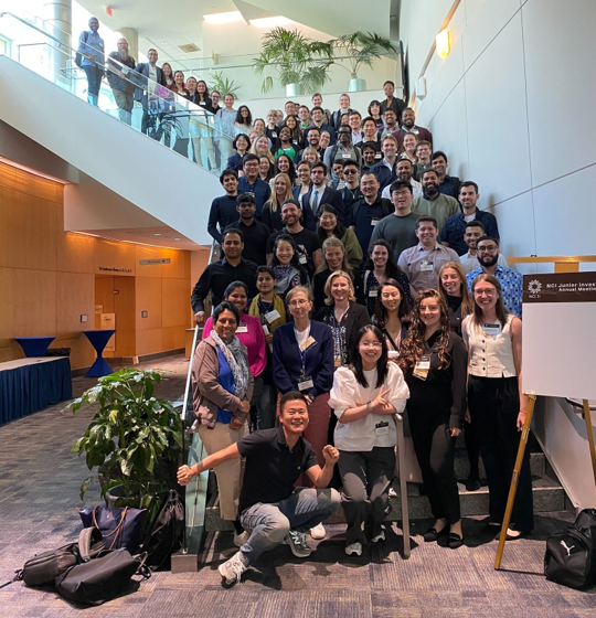 Group photo showing attendees of the 2024 NCI Junior Investigator Meeting on the stairs of the conference center