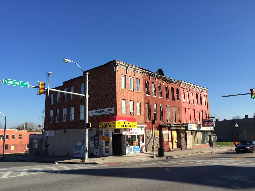 Image of abandoned rowhouses in Baltimore, Maryland. A small grocery store sits at the corner of the building. 