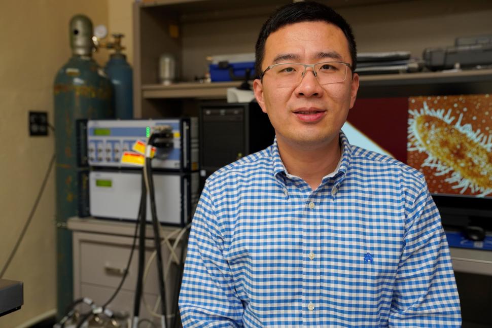 Photo of Dr. Congzhou Wang with a biological image on a computer screen behind him. 