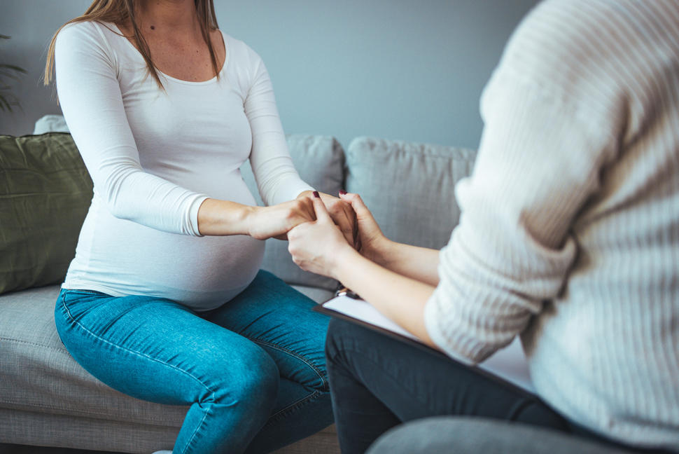 A woman with a clipboard holding the hands of a pregnant woman.