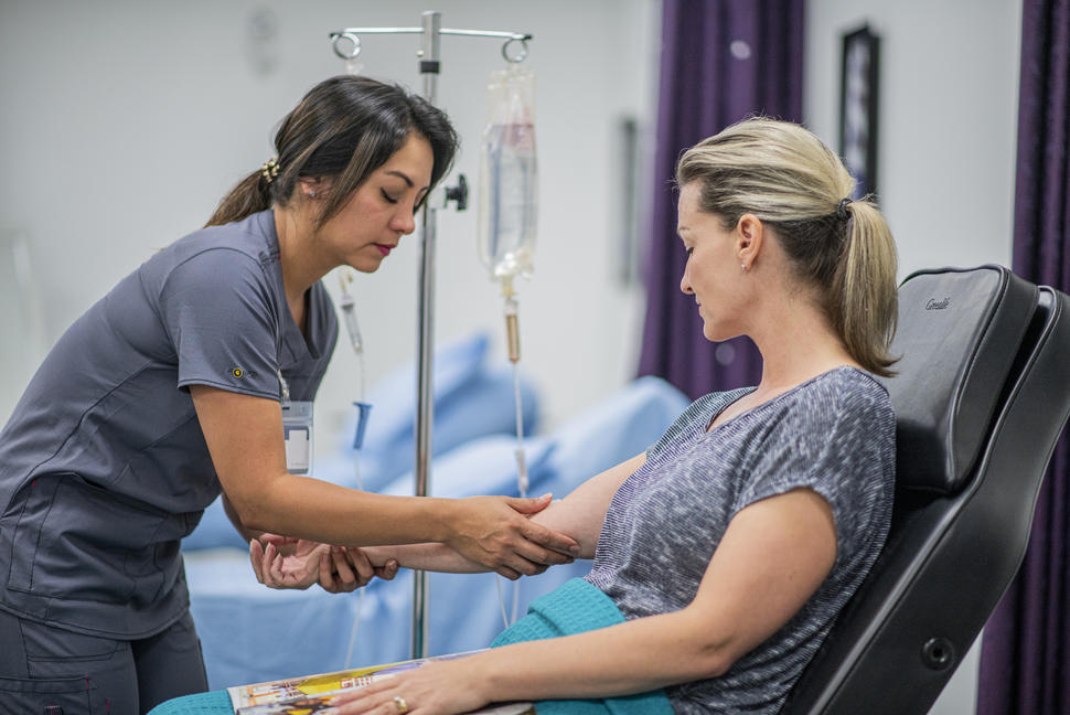 A health professional checking a patient's arm as she sits in a hospital bed.