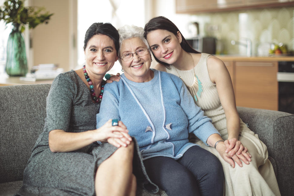 A senior woman sitting in between an older woman and a younger woman on a sofa.