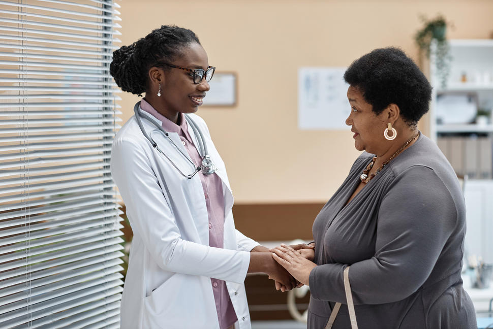 A doctor smiling and holding patient's hands while the patient talks to her.