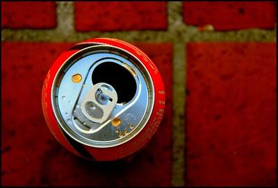 A photo of a red soda can, taken from directly above, sitting on a dark red tiled floor.