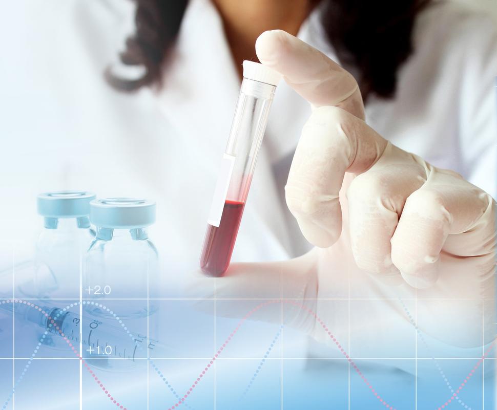 A gloved hand holds a test tube half-filled with blood vertically between the index finger and thumb.