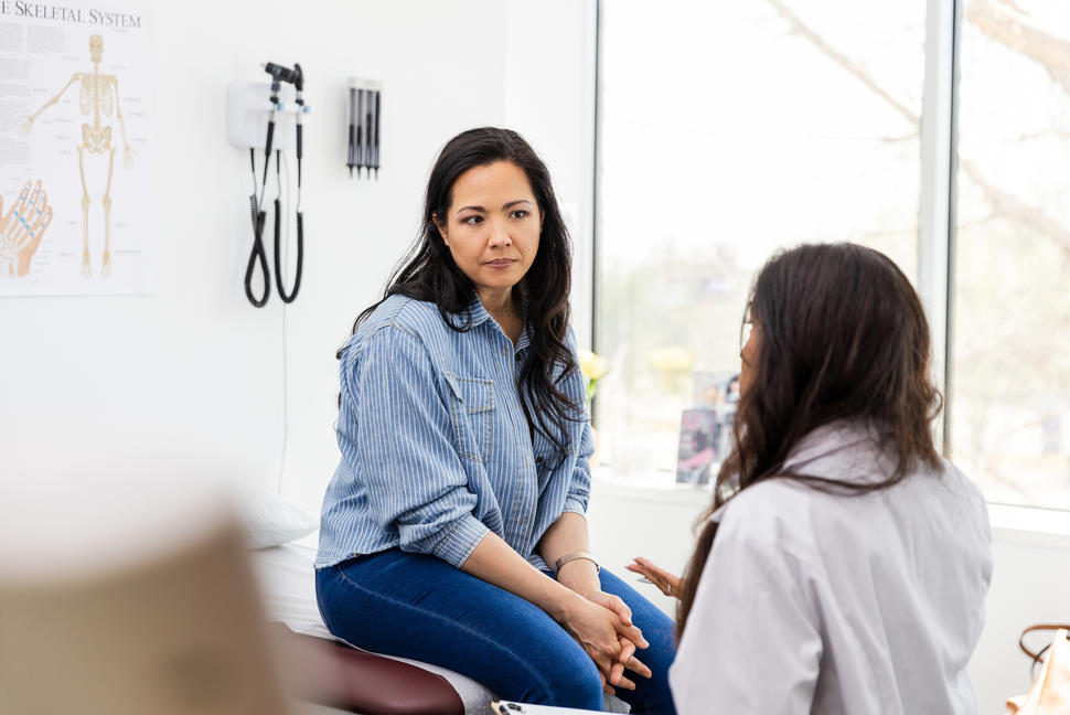 A middle-aged women sitting in a doctor's office speaking with the doctor.