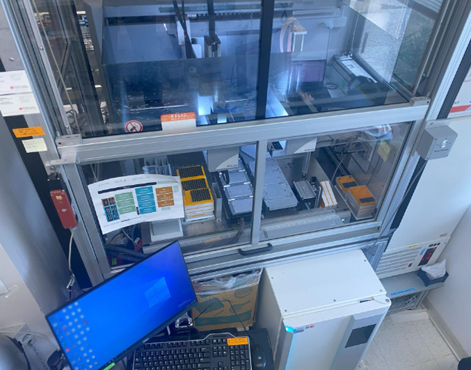 Immunotron is a robotics-machine learning platform. Image shows the computer screen on the right and robotics machinery in the background. 